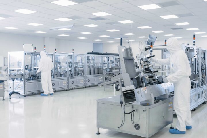 Sterile semiconductor lab with 2 fully covered scientists in white protective gear.