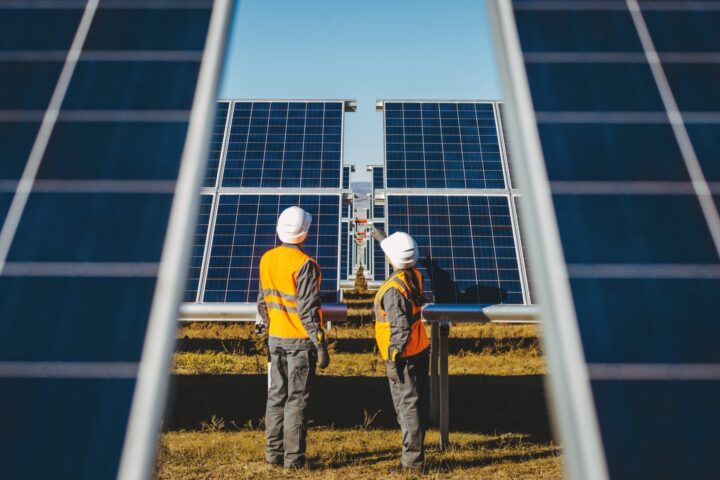 2 service operators in orange vests and hard hats looking at solar panels