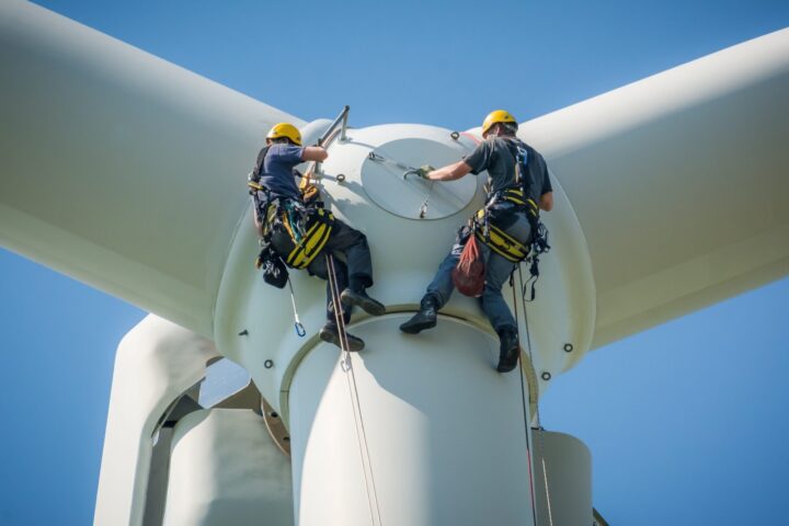 Close up picture of wind turbine with 2 workers in safety gear operating on the wind turbine