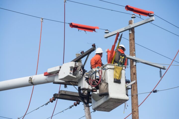 2 Power linemen in hardhats in operating box next to power lines
