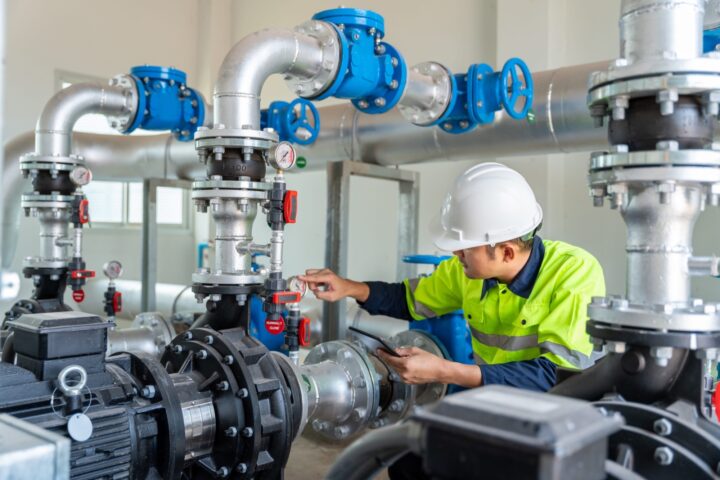 Equipment technician with a hard hat on operating on industrial utility pipes