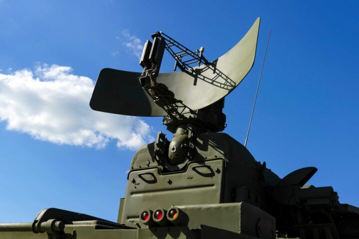 Green military-grade satellite pointing upwards with a blue sky and a cloud in the background